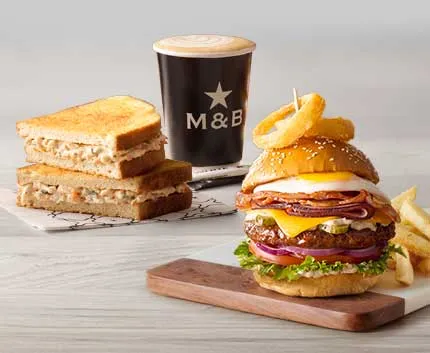 A burger and coffee placed on a wooden table with toasted sandwich