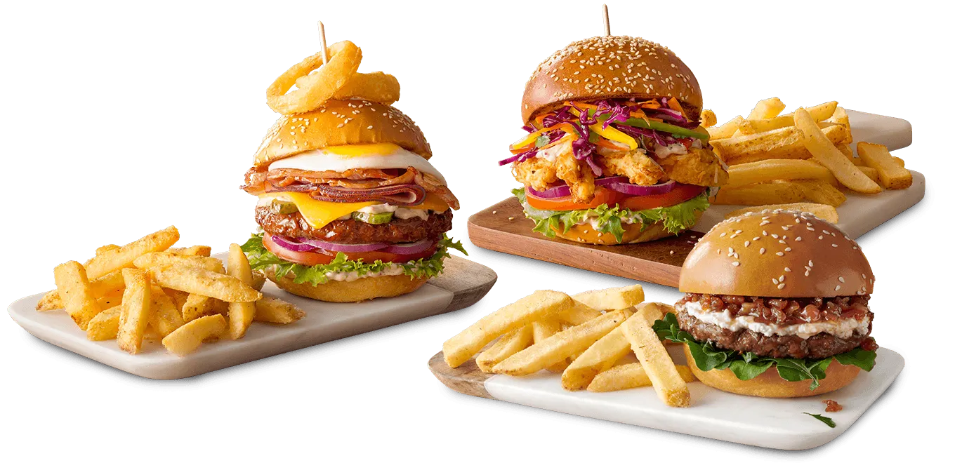 A variety of gourmet burgers presented on a rustic wooden table with assorted toppings and sides