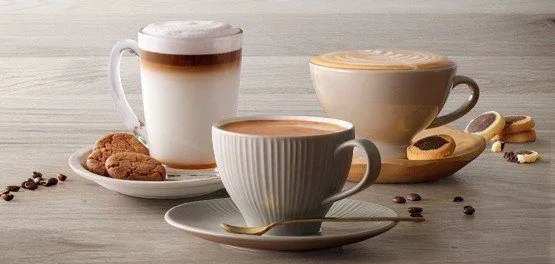 Coffee cups with latte art on a wooden table surrounded by beans