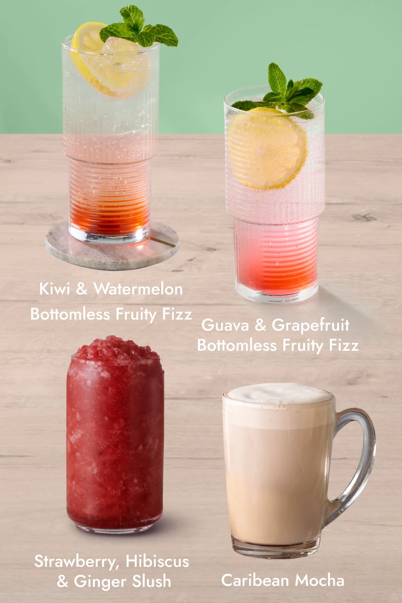 Five different drinks on a wooden surface with a green background: Hot Chocolate, Guava & Grapefruit Bottomless Fruity Fizz, Strawberry & Hibiscus Ginger Slush, Pear & Elderflower Bottomless Fruity Fizz, and a new Rolo Muggachino with whipped cream and chocolate drizzle.