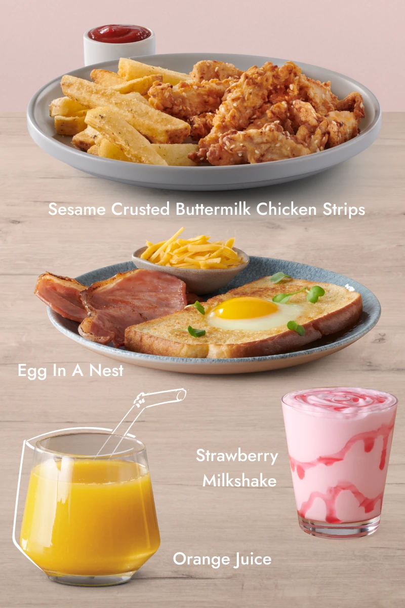 Three food and drink items on a wooden surface with a pink background: a plate of Sesame Crusted Buttermilk Chicken Strips with fries and ketchup, a glass of orange juice, and a plate of Egg In A Nest with grilled ham and a bowl of grated cheese.