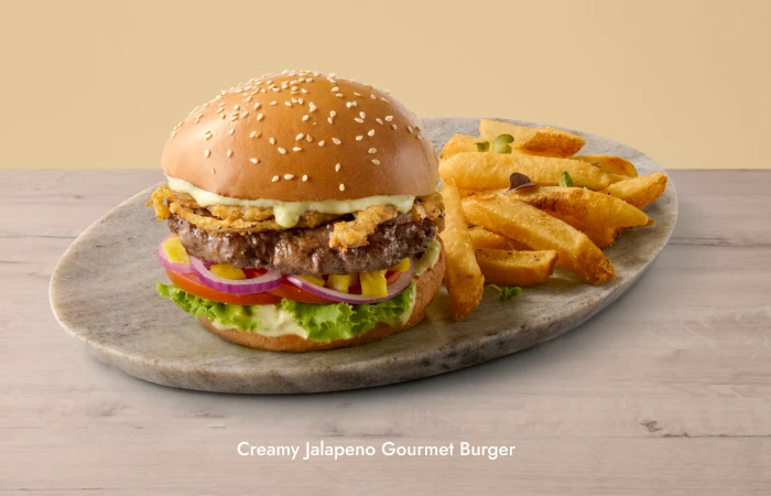 Creamy Jalapeno Gourmet Burger served on a sesame seed bun with lettuce, onions, and sauce, accompanied by thick-cut fries on a stone serving plate.