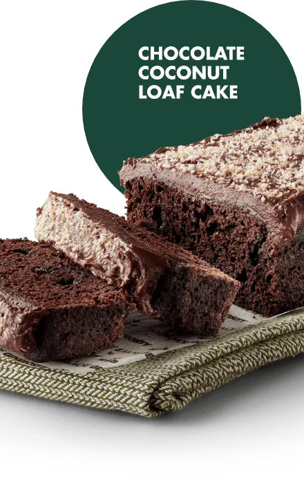 A moist chocolate loaf cake topped with shredded coconut, served on a white plate